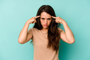 Young caucasian woman isolated on blue background focused on a task, keeping forefingers pointing head.