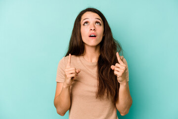 Young caucasian woman isolated on blue background pointing upside with opened mouth.