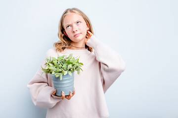 Caucasian teen girl holding a plant isolated on blue background touching back of head, thinking and making a choice.