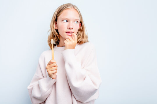 Caucasian teen girl holding a toothbrush isolated on blue background relaxed thinking about something looking at a copy space.