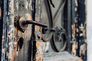 Closed aged door made of wood that is worn or weathered with an iron handle