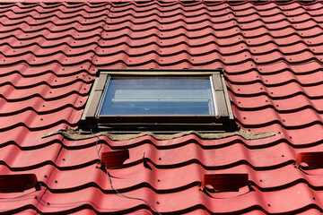 Close up to an attic window mounted on a roof with new red tiles