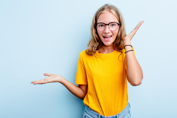 Caucasian teen girl isolated on blue background holds copy space on a palm, keep hand over cheek. Amazed and delighted.