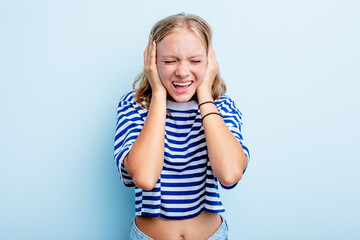 Caucasian teen girl isolated on blue background covering ears with hands trying not to hear too loud sound.