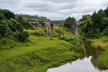 Obraz premium Small railway bridge over small river near Manjakandriana, Madagascar, green grass and trees around. There is only small number of railroads on whole island