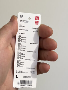 London, United Kingdom - Jan 3, 2022: POV male hand holding price tag for the new Uniqlo Pile Lined fleece zip jacket with composition and country of origin made in china