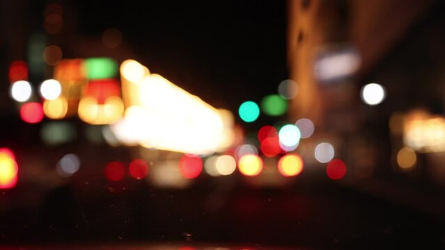 Neon, traffic and road lights blink out of focus seen through filthy glass