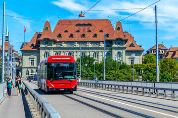 Fototapeta na wymiar BERN, SWITZERLAND - August 2nd 2022: The red bus on the Kirchenfeld Bridge over the Aare River. Public transport.