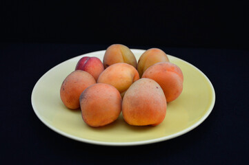 yellow plate with ripe apricots on a dark background. Useful fruit. Pineapple apricots on a black background. Healthy and delicious nutrition for weight loss and during dieting