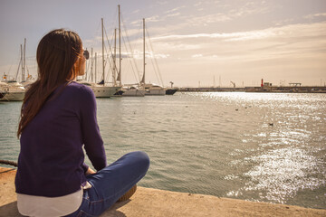 Chica joven sentada mirando el mar en un puerto pesquero 
