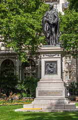 London, UK - July 4, 2022: Whitehall Gardens.  Black bromze Sir Henry Bartle Edward Frere statue on stone pedestal with Pro Patria mural backed by green foliage. Lawn and yellow flowers.