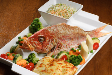 Fried fish with vegetables on wooden table.