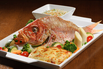 Fried fish with vegetables on wooden table.