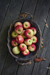 Autumn apples in a basket on a grey wood backdrop with fall leaves