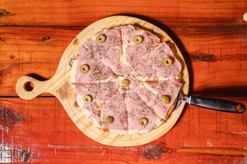 Overhead view of a mozzarella pizza with ham on a wooden table.