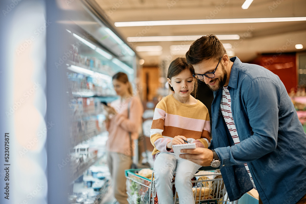 Wall mural happy father and his daughter going through list of groceries while buying in supermarket.