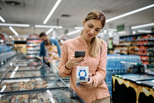 Smiling woman scanning QR code on product while buying in supermarket.
