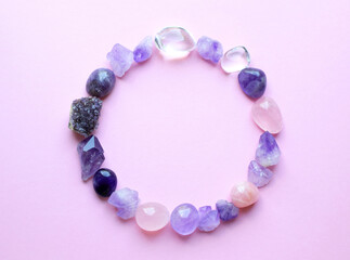 The circle is lined with natural minerals. Semi-precious stones of different colors in raw and processed form. Amethyst crystals, rose quartz and rock crystal on a pink background.