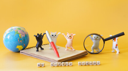 Funny toy dancing kittens from meme, notebook, pen, globe and magnifier on yellow, next to the inscription My little school. Concept of didactic game about school. Preparing for schooling. - obrazy, fototapety, plakaty