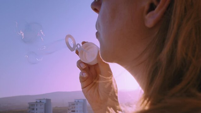 woman blows soap bubbles from a balcony at sunset against the backdrop of mountains