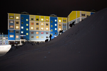 Winter evening in a northern city in the Arctic. Children climb a snowy hill to ride from it....