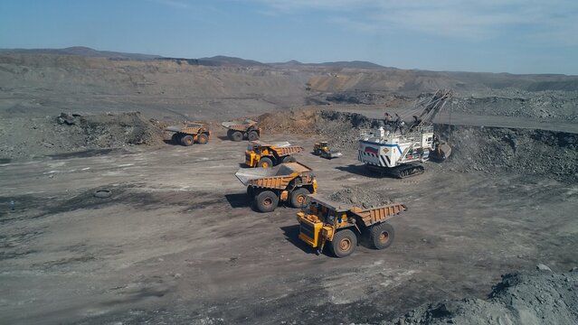 Group of technological transport around huge mining excavator. Two dump trucks and small loader. Aerial view