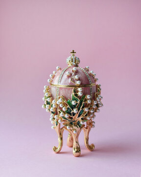 A traditional Russian souvenir in the Faberge style, an enamel pink gilded egg adorned with precious crystals and pearls, a copy of the famous Faberge egg "Lilies of the valley".