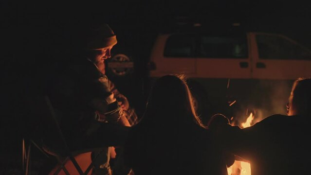 Goup of friends campers sits near the bonfire at night