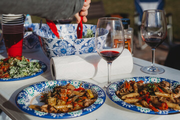 picnic with grilled chicken with vegetables on paper plate with glasses of wine and salad bowl 