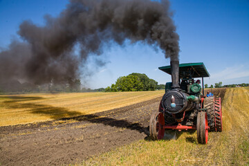 an old steam tractor with smoke billowing plows a farm field