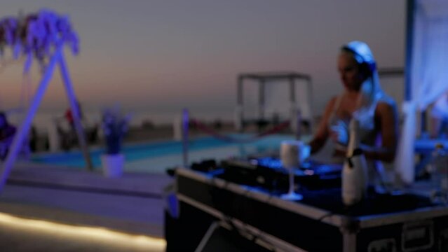 Blurry: Female DJ with a large cleavage playing music at beach bar after sunset