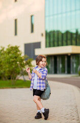 a little schoolgirl, standing in glasses,near the school building,with a backpack