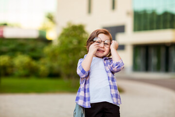 Fototapeta premium a little schoolgirl, standing in glasses,near the school building,with a backpack