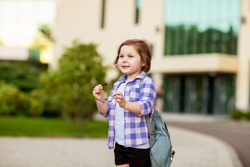 a little schoolgirl, standing in glasses,near the school building,with a backpack