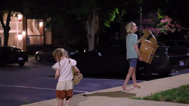 Happy kids walk down the night street to throw cardboard boxes into the recycle dumpster. make the world a better place.