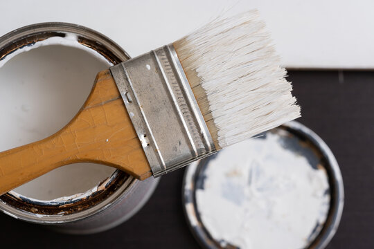 primer plano de brocha con bote de pintura blanca y fondo blanco