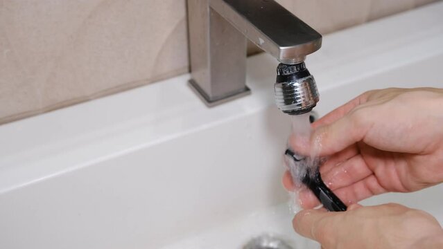 Cleaning shaving razor in bathroom sink. Rinsing off razor with water