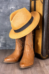 Leather cowgirl boots with a straw hat pattern and an old suitcase stand on the floor against a...