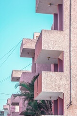 Fototapeta na wymiar pink building with balconies, palm tree between modules, light cables in the space