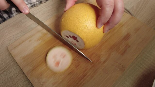 Woman's hands cut grapefruit on the board