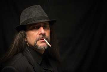 Portrait of middle aged man wearing black clothes and black hat smoking cigarette in the studio