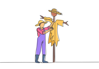 Continuous one line drawing a young male farmer in a straw hat is putting up a scarecrow to keep out pests of birds. Farming minimalist concept. Single line draw design vector graphic illustration.