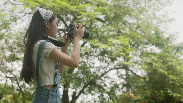 Beautiful happiness young asian woman using camera take a photo for relax in the park, hobby of girl doing shoot picture in the garden, exploration and shot photo, lifestyles and activity concept.
