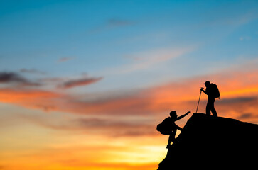 Silhouette two with backpack is climbing a cliff at sunrise. He had an effort to climb all the way...