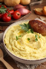 Bowl of tasty mashed potatoes with parsley, black pepper and cutlet served on wooden table, closeup