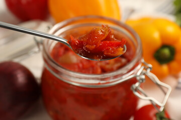 Spoon with delicious lecho over jar, closeup