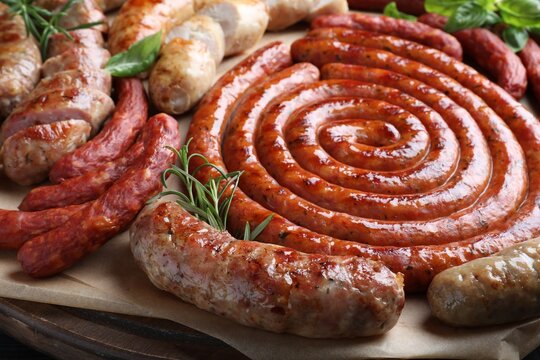 Different delicious sausages with herbs on wooden board, closeup. Assortment of beer snacks