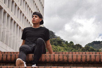 Chico vestido de negro deportivo sentado en los escalones con un edificio de fondo - Bogotá, Colombia