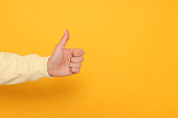 Woman showing thumb up on orange background, closeup. Space for text