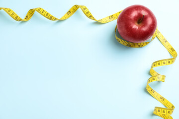 Fresh red apple with measuring tape on light blue background, flat lay. Space for text